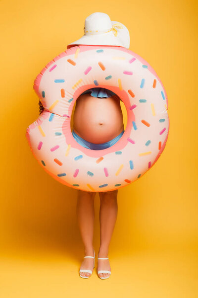 беременная женщина в соломенной шляпе прячется за купальным кольцом на желтом