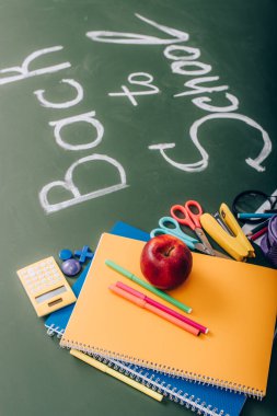 Okul malzemelerinin seçici odak noktası ve okula yakın taze elma yeşil karatahta metni