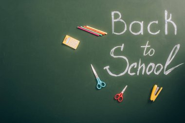 top view of back to school inscription near school stationery on green chalkboard with copy space clipart