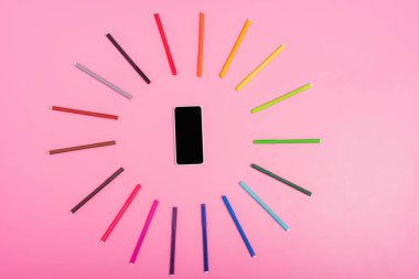 top view of smartphone with blank screen framed by multicolored felt-tip pens on pink clipart