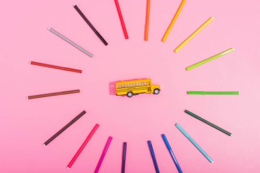 top view of school bus model framed by color felt pens on pink  clipart