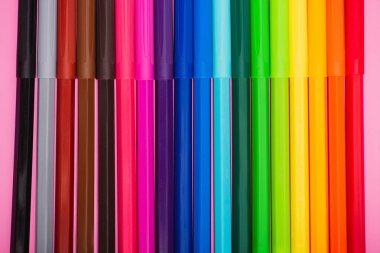 top view of multicolored felt-tip pens row on pink background clipart