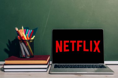 KYIV, UKRAINE - 7 Temmuz 2020: Netflix web sitesi ile birlikte yeşil karatahtanın yanındaki kitap yığınının üzerinde kağıt tutacağı