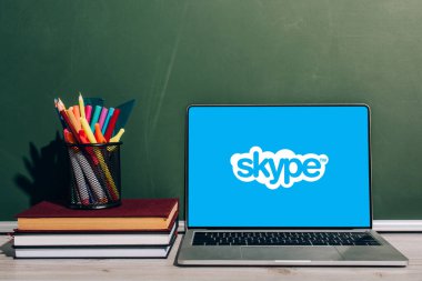 KYIV, UKRAINE - 7 Temmuz 2020: Yeşil karatahtanın yanında istiflenmiş ders kitaplarına sarılı kalem tutacağı ile Skype web sitesi