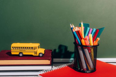 Okul otobüsü modeli, yeşil karatahtanın yanındaki not defterinde kalem tutacağının yanındaki kazıklı kitaplarda.