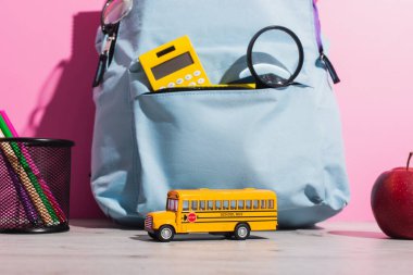 Okul otobüsü modelinin yanında mavi çanta, olgun elma ve keçeli kalemle keçeli kalem.