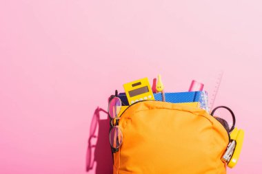 Okul kırtasiyesi ve pembe gözlüklerle dolu sarı sırt çantası.