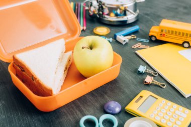 Sandviçli yemek kutusunun seçici odağı ve kara karatahtanın üzerinde okul malzemelerinin yanındaki elma.