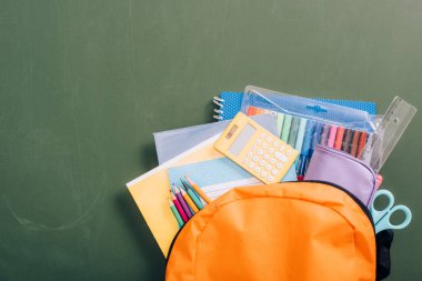 Yeşil karatahtanın üzerinde okul malzemeleriyle dolu sarı sırt çantasının üst görüntüsü