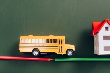 Okul otobüsü ve yol üzerindeki yeşil karatahta kalemlerden yapılmış ev modellerinin üst görüntüsü.