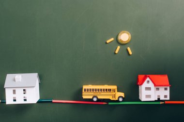 Ev modellerinin üst görüntüsü, yoldaki oyuncak okul otobüsü, renkli kalemlerden yapılmış, ve yeşil karatahtadaki mıknatıslardan yapılmış güneş.