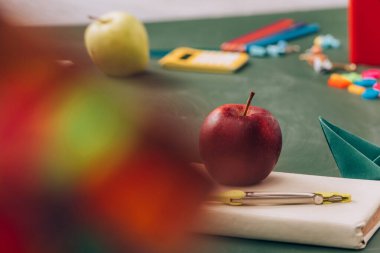 Elma ve pusula ayırıcısının seçici odak noktası yeşil karatahtanın üzerindeki okul malzemelerinin yanındaki kitap. 
