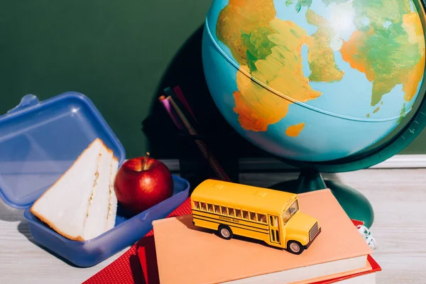 globe near lunch box and school bus model on books near green chalkboard