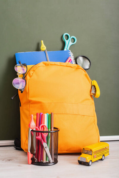 школьный рюкзак полный канцелярских принадлежностей возле держателя ручки и модели школьного автобуса