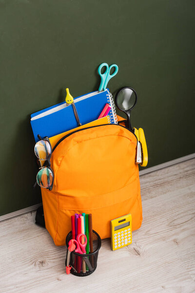 высокий угол просмотра желтого рюкзака со школьными принадлежностями рядом с калькулятором и держателем ручки