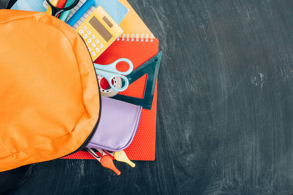 top view of yellow backpack with school stationery on black chalkboard, panoramic shot