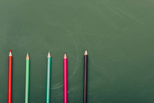 top view of row of multicolored pencils on green chalkboard