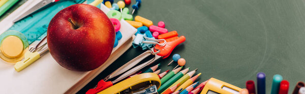 selective focus of delicious apple on book and school stationery on green chalkboard, panoramic concept