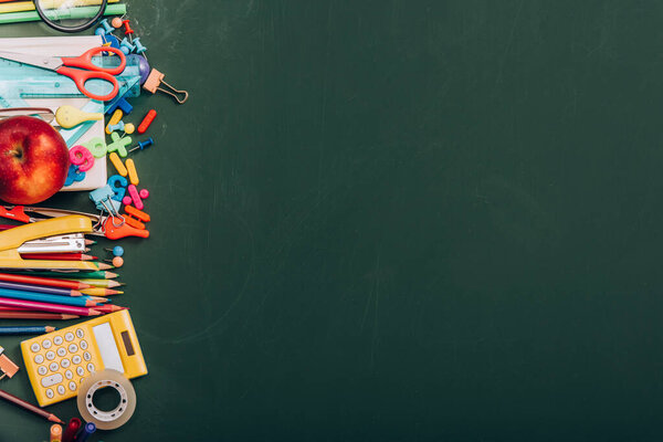 top view of ripe apple, calculator and school stationery on green chalkboard with copy space