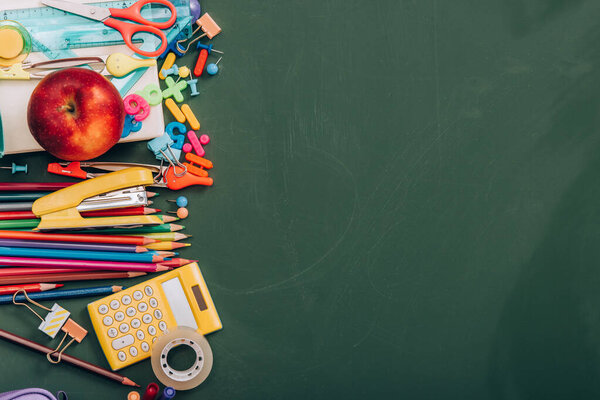 top view of ripe apple, calculator and school stationery on green chalkboard with copy space