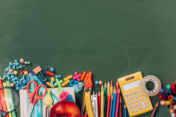top view of apple, calculator and school supplies on green chalkboard