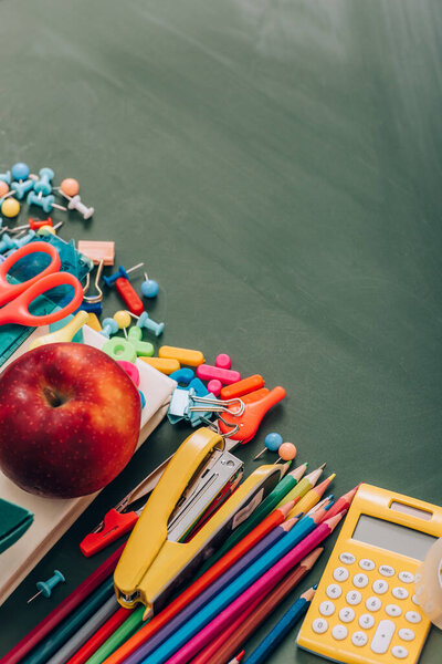 high angle view of ripe apple on book near school stationery on green chalkboard