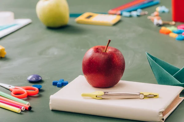 有选择地把成熟的苹果放在书本上 靠近学校的文具放在绿色黑板上 — 图库照片