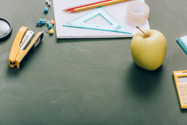 ripe apple, copy book and school supplies on green chalkboard