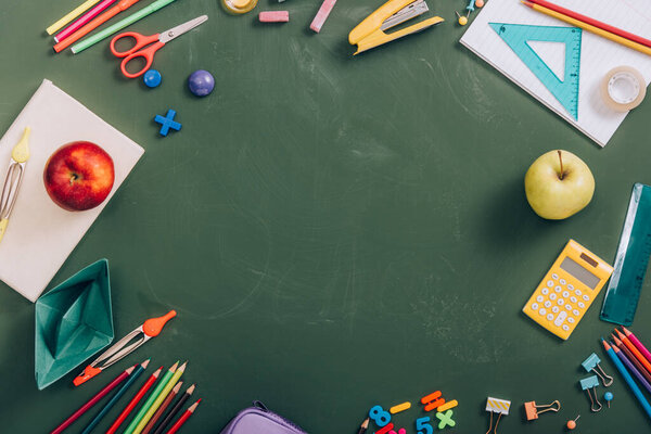 top view of frame with school supplies, ripe apples and paper boat on green chalkboard