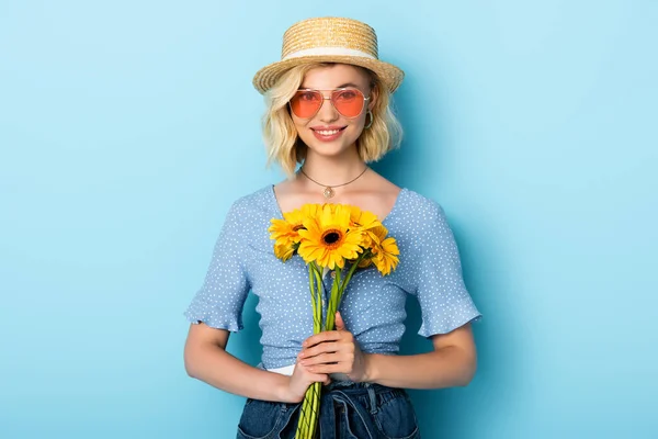 Γυναίκα Ψάθινο Καπέλο Και Γυαλιά Ηλίου Κρατώντας Λουλούδια Στο Μπλε — Φωτογραφία Αρχείου