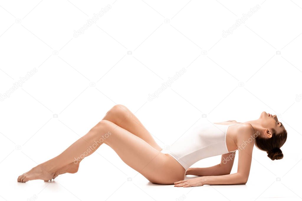 side view of barefoot woman in bodysuit lying on white 