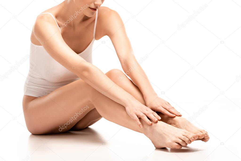 partial view of barefoot woman in bodysuit touching legs while sitting on white