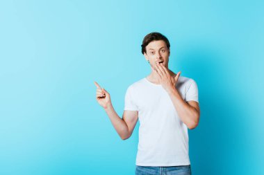 Excited man in white t-shirt pointing with finger on blue background clipart