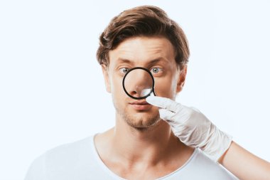 Lateks eldivenli dermatolog, beyaz tenli hastanın burnunun yanında loupe tutuyor.