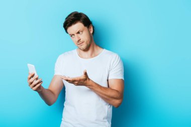 Mavi arka plandaki akıllı telefonu işaret eden ciddi bir adam.