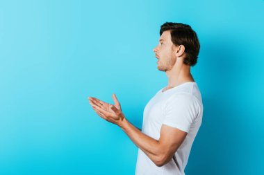 Elleriyle işaret eden ve mavi arka plana bakan heyecanlı adamın yan görüntüsü