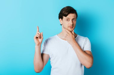 Beyaz tişörtlü genç adam mavi arka plan hakkında fikir sahibi.