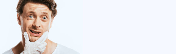 Панорамный снимок дерматолога в латексной перчатке касающегося подбородка испуганного пациента, изолированного на белом