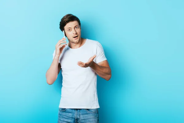 Young Man Pointing Hand While Talking Smartphone Blue Background — Stock Photo, Image