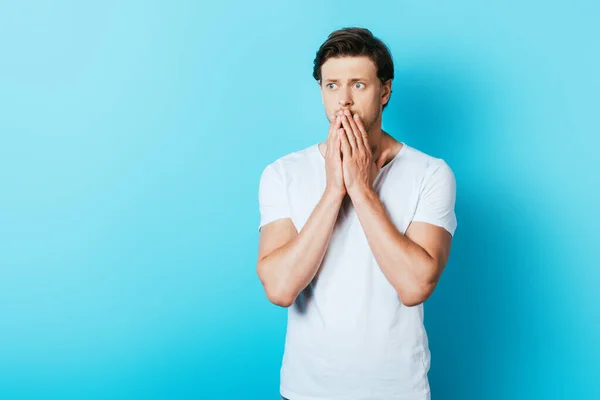 Sad man with hands near mouth looking away on blue background