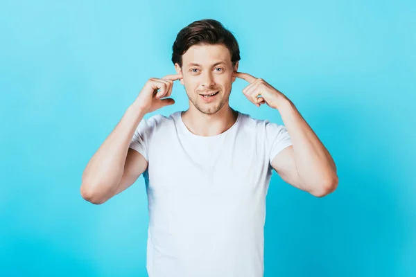 Young Man Looking Camera While Covering Ears Fingers Blue Background — Stock Photo, Image