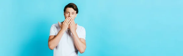 Panoramaorientering Chockad Man Täcker Munnen Med Händerna Blå Bakgrund — Stockfoto