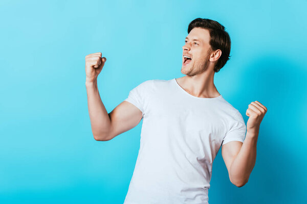 Young man in white t-shirt showing yes gesture on blue background