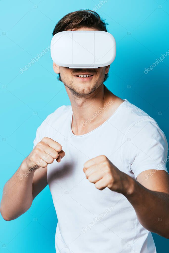 Young man in virtual reality headset showing fists on blue background