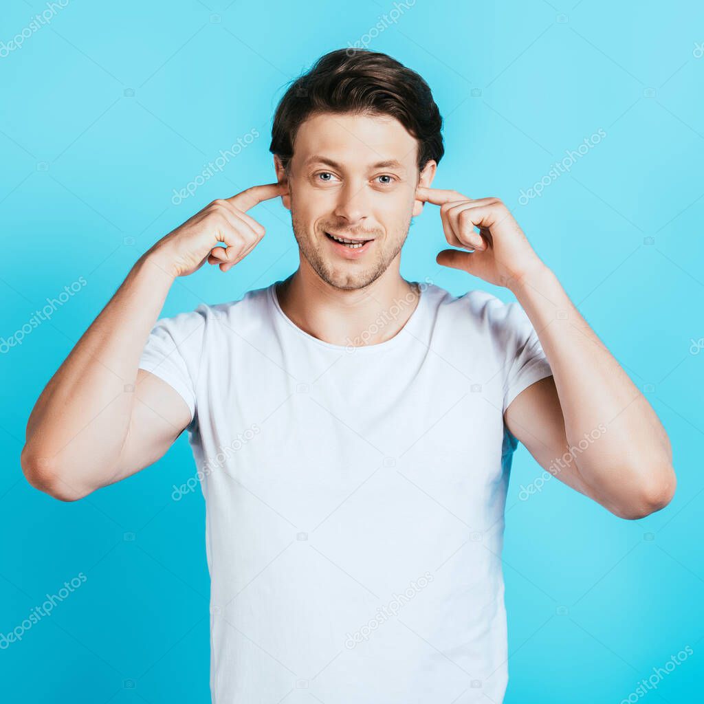 Man in white t-shirt covering ears with fingers on blue background