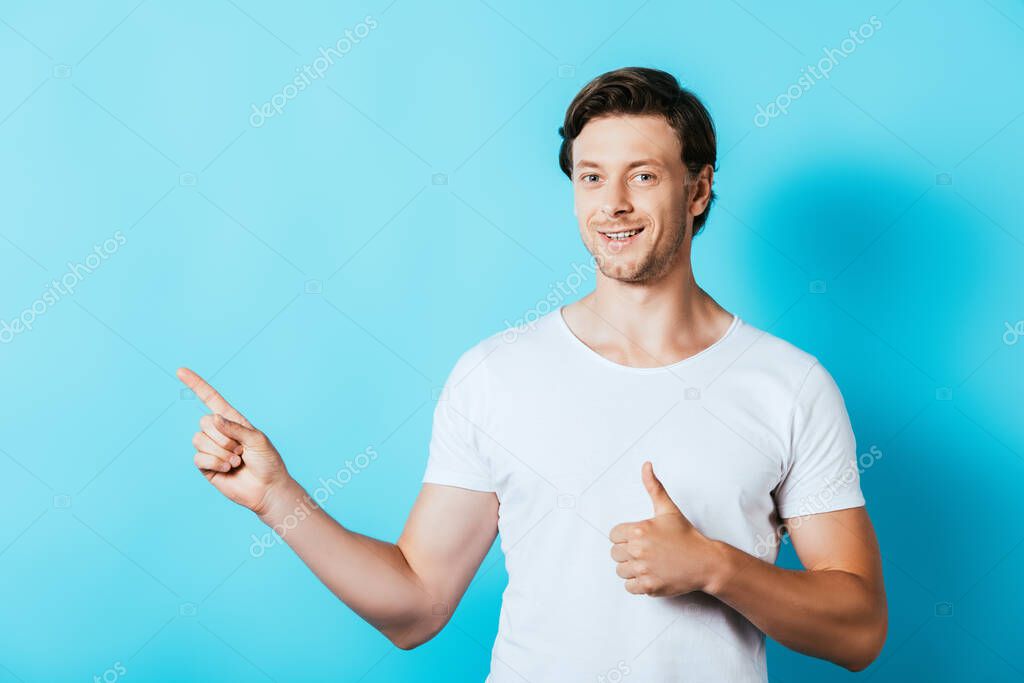 Young man in white t-shirt pointing with finger and showing like gesture on blue background