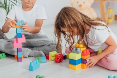 Erkek çocuğun, kız kardeşinin yanında pijamalarıyla otururken inşaat bloklarıyla oynadığı görüntüler.