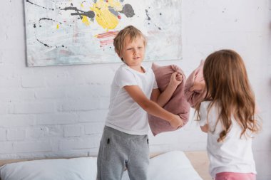 Pijamalı kardeşler yatak odalarında yastıkla kavga ederken eğleniyorlar.