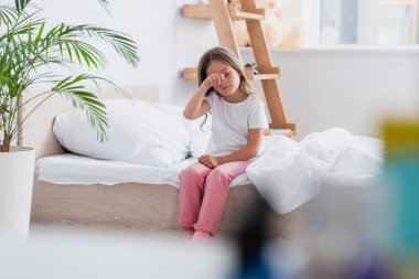 Uyanmış kızın pijamalarıyla yatakta otururken gözüne dokunduğu seçici odak.