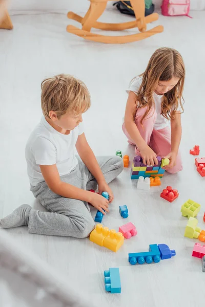 Visão Alto Ângulo Irmãos Concentrados Pijama Sentado Chão Brincando Com — Fotografia de Stock